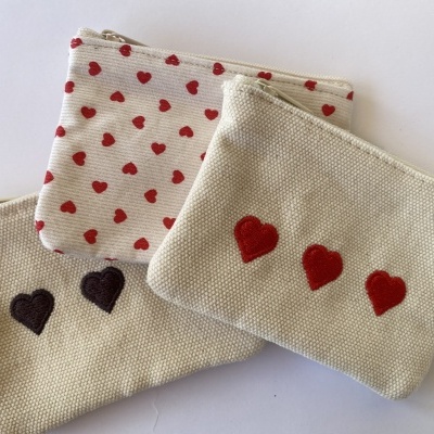 Três pequenas bolsas de tecido com fecho e corações bordados ou estampados.