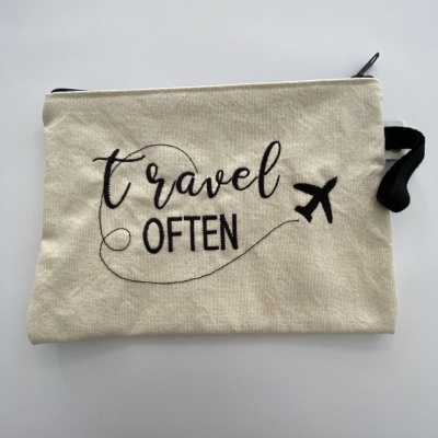 Bolsa de tecido bege com texto 'travel OFTEN' e desenho de avião preto