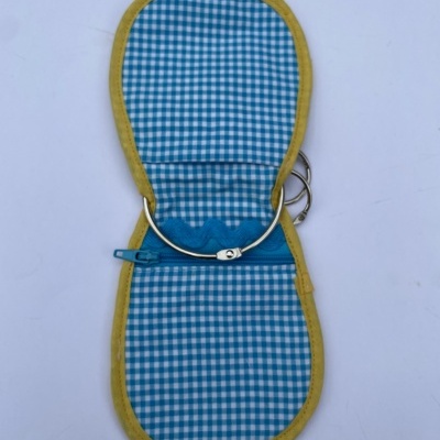 Porta-óculos xadrez azul e branco com bordas amarelas e fecho éclair azul aberto sobre fundo branco