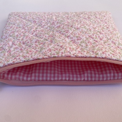 Bolsa acolchoada rosa com padrão floral e interior de quadrados rosa.