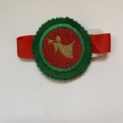 Broche verde, vermelho e dourado com figura de anjo, em fita vermelha e branca
