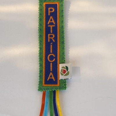 Marcador de livros em feltro verde com texto PATRÍCIA em azul e amarelo e fitas coloridas