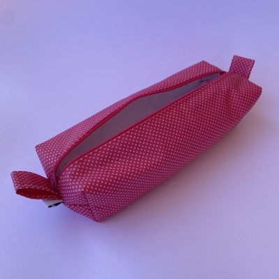 Estojo retangular cor-de-rosa com padrão de pontos brancos e fecho de correr vermelho aberto.
