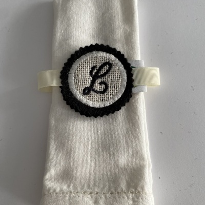 Guardanapo branco com argola decorativa preta e branca com letra 'L'
