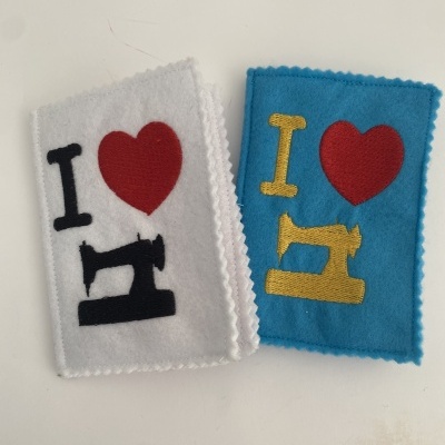 Dois retângulos de feltro com bordados de máquina de costura e coração, um em branco e outro em azul.
