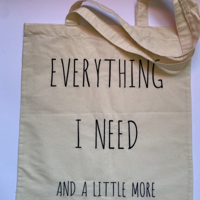 Saco de algodão bege com texto preto 'EVERYTHING I NEED AND A LITTLE MORE' em fundo branco.