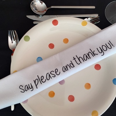 Prato com pontos coloridos, guardanapo branco com texto em inglês, talheres e fundo preto com texto em português.