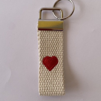 Porta-chaves de tecido bege com coração vermelho bordado e suporte metálico prateado