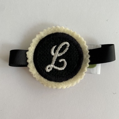 Prendedor de cabelo com fita preta e aplique redondo em feltro com a letra L