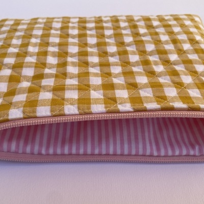 Estojo acolchoado amarelo e branco com fecho rosa aberto mostrando interior listrado