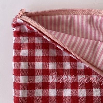 Bolsa de tecido xadrez vermelha e branca com fecho cor de rosa e forro riscado rosa e branco.