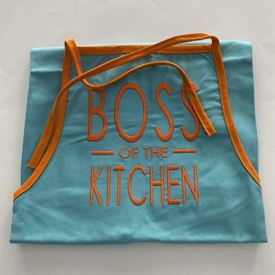 Avental azul claro com bordados e fitas laranja com texto 'BOSS OF THE KITCHEN'
