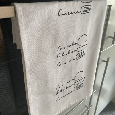 Pano de cozinha branco com texto e ilustração a preto pendurado em puxador de forno