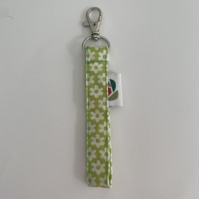 Porta-chaves com fita verde e flores brancas e fecho metálico