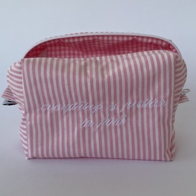 Necessaire rosa e branca com riscas e texto bordado.