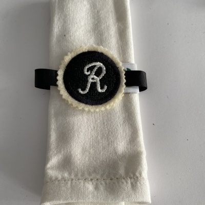 Guardanapo branco com fita preta e distintivo com a letra 'R'