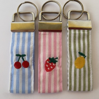 Três porta-chaves de tecido riscado com frutas bordadas e argolas metálicas