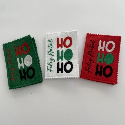 Três tecidos quadrados com texto natalício HO HO HO e Feliz Natal em verde, branco e vermelho