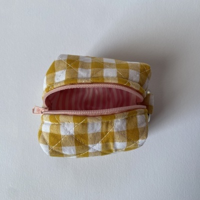 Bolsa pequena xadrez em tecido amarelo e branco com fecho rosa e interior às riscas rosa.