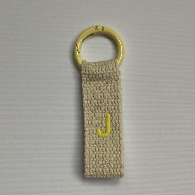 Chaveiro com argola amarela e fita têxtil bege com letra J