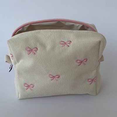Bolsa pequena bege de tecido com laços rosa bordados e fecho rosa