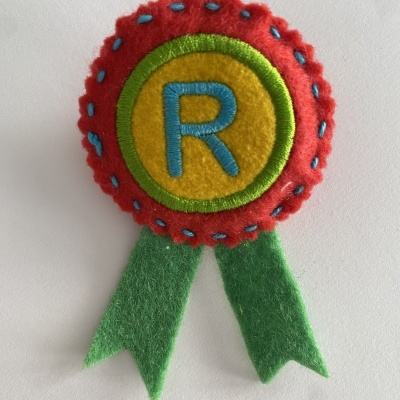 Distintivo em feltro colorido com letra R e fitas verdes