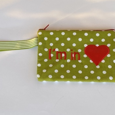Carteira pequena verde com bolas brancas, zíper vermelho, alça riscada e texto 'I'm in' com coração vermelho