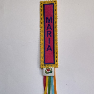 Marcador de tecido com nome Maria bordado, detalhes coloridos e fitas penduradas