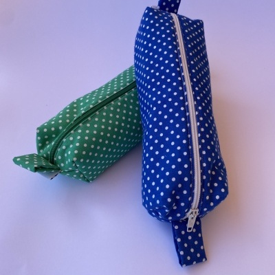 Dois estojos retangulares com padrão de bolinhas brancas, um azul e outro verde, ambos com fecho