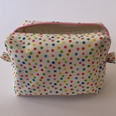 Necessaire branca de tecido com padrão de bolinhas coloridas e fecho de correr cor-de-rosa.