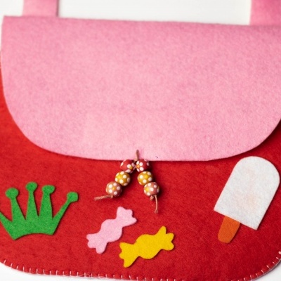 Mala infantil em feltro rosa e vermelho com decoração de coro verde, doces e gelado.