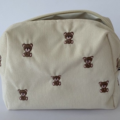 Mala creme com bordados de ursinhos castanhos sobre tecido canelado