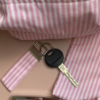 Chave preta com porta-chaves de tecido às riscas rosas e brancas rodeada de itens femininos cor-de-rosa.