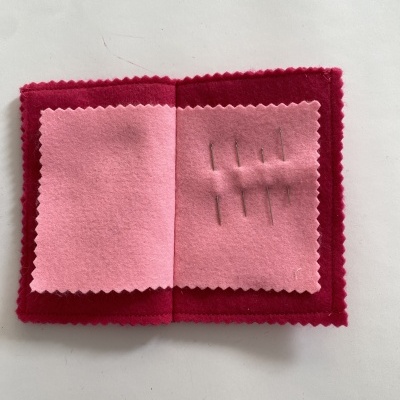 Estojo de feltro vermelho e rosa aberto com agulhas de costura