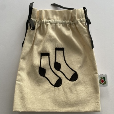 Saco de tecido bege com desenho de meias pretas e cordões escuros