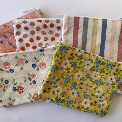 Cinco pequenas bolsas de tecido com padrões florais e riscas, todas com fecho branco, dispostas sobre superfície branca.