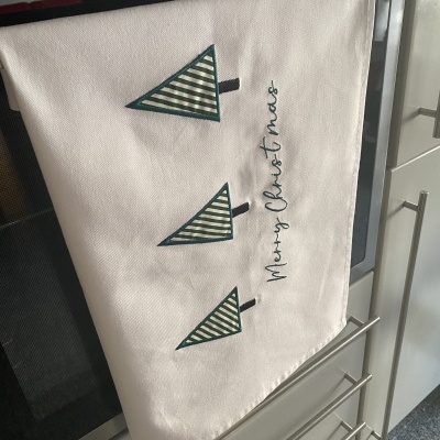 Pano de cozinha branco com árvores de Natal verdes bordadas e texto Merry Christ mas