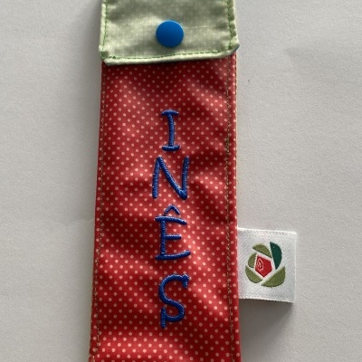 Estojo de tecido vermelho com pontos brancos e aba verde claro com botão azul e nome INÊS bordado