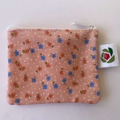 Estojo pequeno de tecido salmão com flores azuis e rosas, fecho branco e etiqueta com rosa vermelha