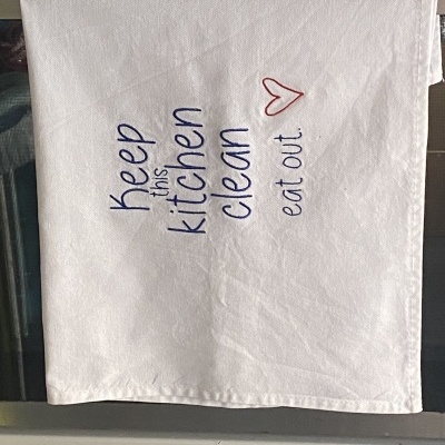 Pano branco bordado com mensagem em inglês e coração vermelho.