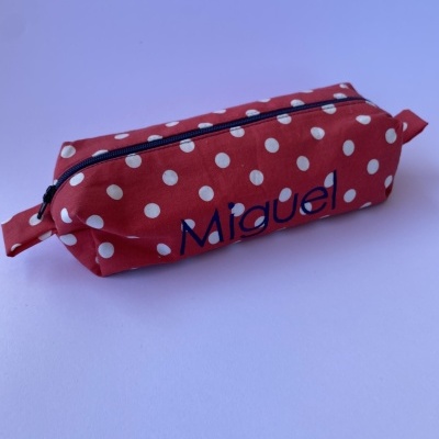 Estojo vermelho com bolinhas brancas e fecho preto com o nome 
