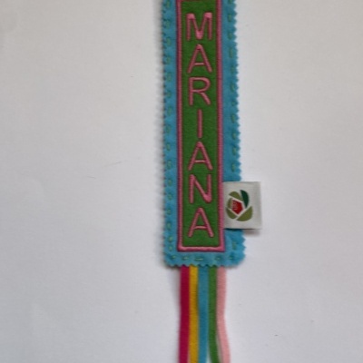 Marca-página de tecido azul claro com nome MARIANA bordado e fitas coloridas penduradas