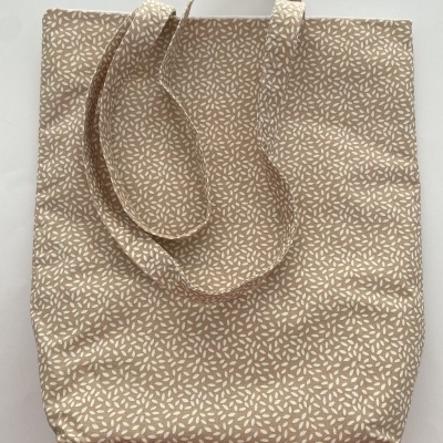 Saco de tecido bege com padrão branco e alças em tecido, sobre superfície branca