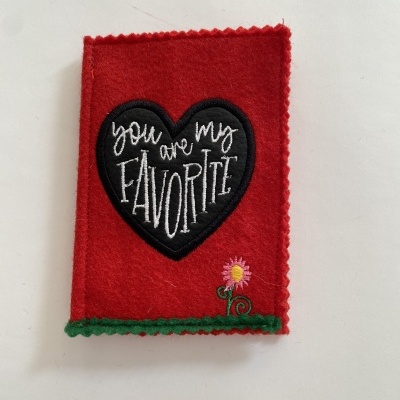 Peça de tecido vermelho com coração preto e texto bordado e pequena flor rosa