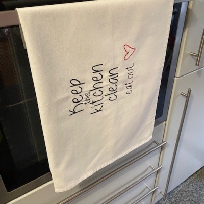 Pano de cozinha branco com texto bordado pendurado em forno