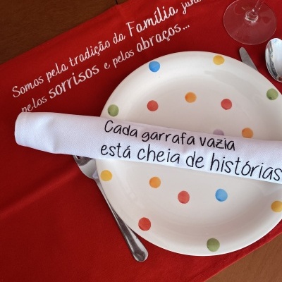 Mesa posta com prato de bolinhas e guardanapo com textos em português, sobre toalha vermelha