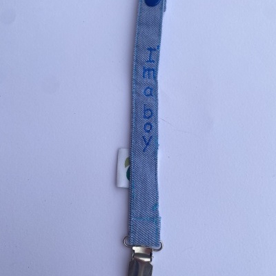 Prendedor de chupeta azul claro com mola metálica e texto 