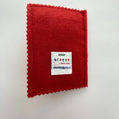 Carteira em feltro vermelho com etiqueta branca costurada com texto. 