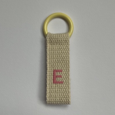 Chaveiro com argola amarela e fita de tecido bege com bordado rosa