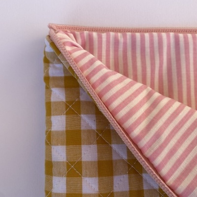 Cobertor ou manta dupla-face com padrão xadrez amarelo e riscas rosas.